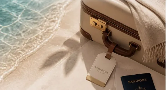 Suitcase, passport and Roam Below luggage tag on white sand